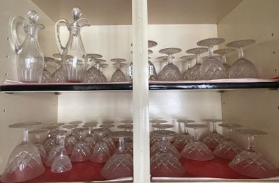 bottles and glasses on a shelf in a cabinet with a red cloth