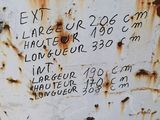 rusted metal container with writing on it sitting on the side of a building