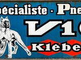 une enseigne indiquant « Spécialiste des pneus V10 Kleber » sur la façade d'un immeuble