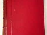 un livre rouge posé sur une table blanche, à côté d'un verre