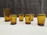 six yellow glass tumblers are lined up on a white table