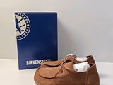 Les chaussures marron se trouvent à côté d'une boîte bleue, posée sur une surface blanche.