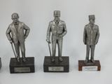 three silver statues of men with hats and canes on wooden bases
