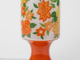 an orange vase with flowers on it sitting on a table