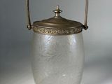 un seau à glace ancien en verre, muni d'une poignée en métal, posé sur une surface blanche