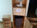 a fan sitting on top of a cabinet next to a trash can