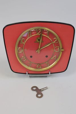 une horloge rouge au cadran doré, à côté d'une clé