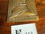 une plaque en laiton représentant une femme portant un foulard, posée sur une table à côté d'un autocollant