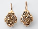 une paire de boucles d'oreilles en or ornées de fleurs et de feuilles sur un fond blanc