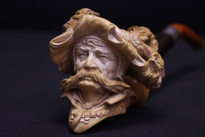 une vieille pipe surmontée d'un visage d'homme coiffé d'un chapeau