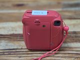 a pink camera on a wooden table with a red cord
