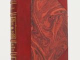 an old book with a red cover sitting on a white surface