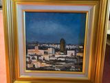 painting of a view of a city in a gold frame on a pink surface