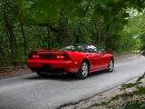 a red sports car driving down the road in the woods