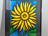 tableau représentant un tournesol jaune dans un cadre noir, posé sur une table