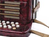 a red accordion sitting on a white surface with a strap around it