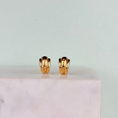 une paire de boucles d'oreilles plaquées or posées sur un bloc de marbre blanc
