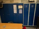several blue lockers in a room with a wooden table and red chair