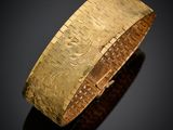 gros plan d'un bracelet en or sur une surface noire