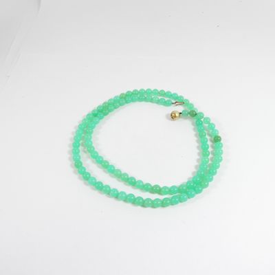un gros plan d'un collier de perles vertes posé sur une surface blanche