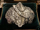 a silver brooch sitting on a velvet cushion on a table