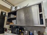 une armoire en acier inoxydable dans la cuisine, sur laquelle sont posées des casseroles et des poêles