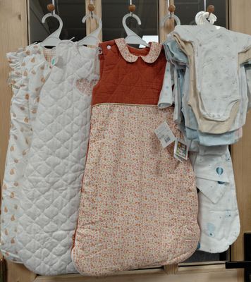 trois vêtements de bébé suspendus à un portant dans une armoire