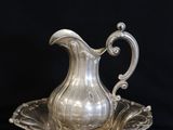 a silver plate with a silver pitcher on it on a black background