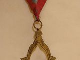 a gold masonic square and compass on a red ribbon