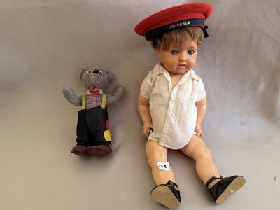une petite poupée assise à côté d'un ours en peluche