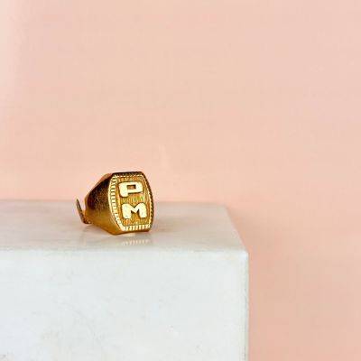 une bague en or sur laquelle est gravée la lettre « f », posée sur un bloc blanc