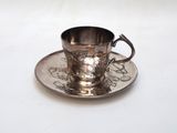a silver cup and saucer sitting on a white table