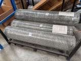 Plusieurs rouleaux de treillis métallique sont empilés sur un rayonnage dans un entrepôt