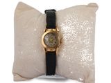 une montre en or avec un bracelet noir posée sur un oreiller