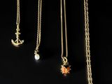 quatre colliers en or ornés de breloques différentes sur fond noir