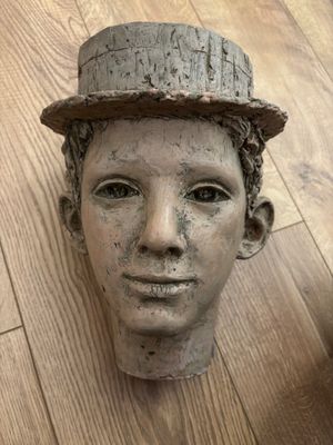 une tête d'homme en argile coiffée d'un chapeau, posée sur un plancher en bois