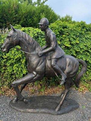 a statue of a man riding a horse in front of a hedge