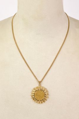 a woman wearing a gold necklace with a sun pendant on it