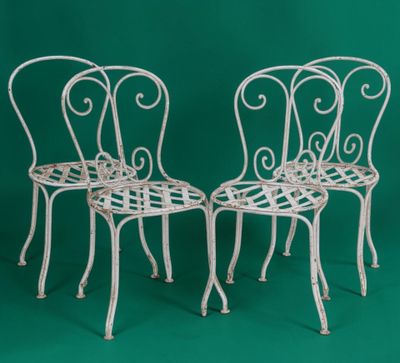two white wrought chairs against a green background
