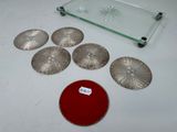 a glass tray with a red lid and six silver coasters