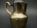 une cafetière ancienne en argent, avec une anse en forme de serpent, sur fond noir