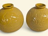 une paire de vases jaunes posés sur une surface blanche, sur fond blanc