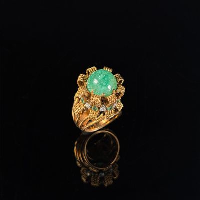 a gold ring with a green stone and diamonds on a black surface