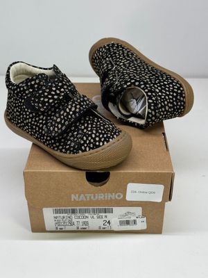 une paire de chaussons de bébé noirs et blancs dans une boîte posée sur une surface blanche