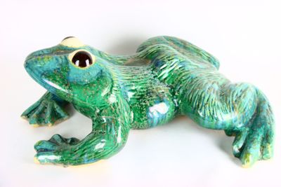une figurine de grenouille verte posée sur une surface blanche