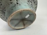 a green vase with black spots on it sitting on a white surface
