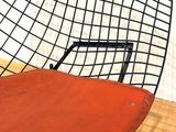 a black wire chair with a red seat on a hard wood floor