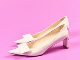 une paire de chaussures blanches ornées de nœuds sur le bout, sur fond rose