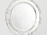 un plat ancien en argent, aux bords festonnés, posé sur un socle