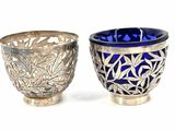 two silver cups with blue glass in them on a white surface